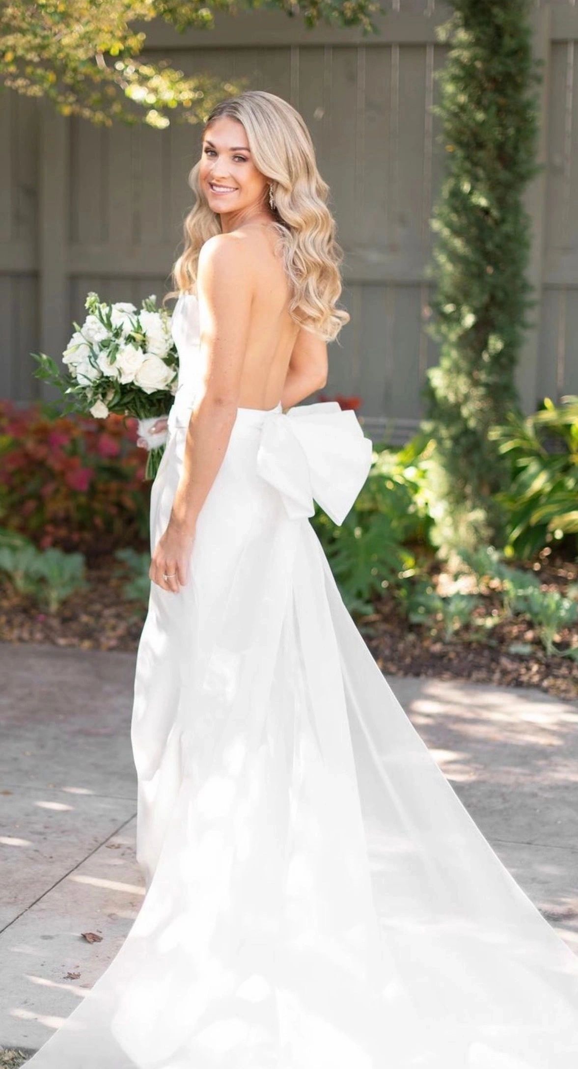 Bride in elegant backless gown with bow detail, garden golden hour