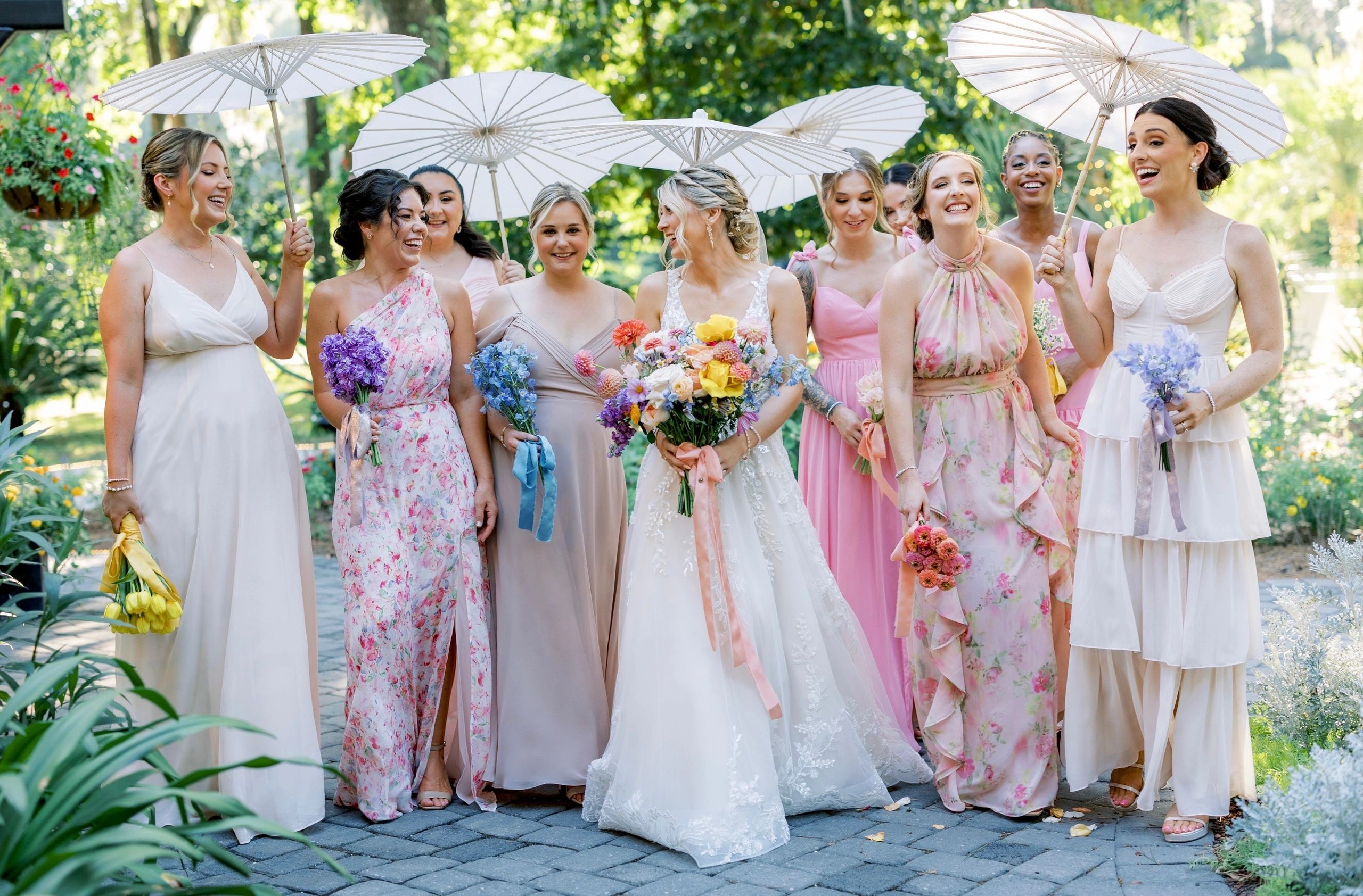 Bridal party of nine women with parasols and bouquets in garden setting