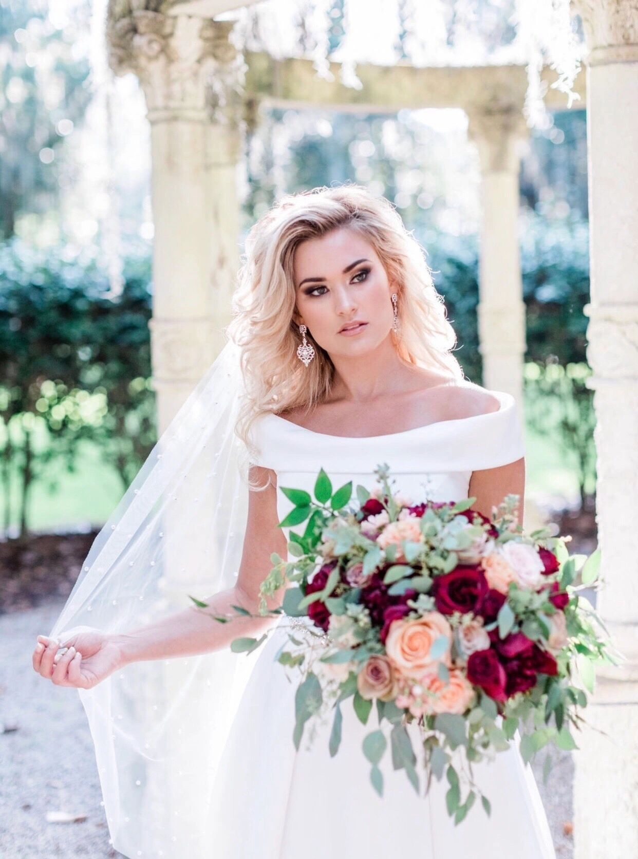 Bride in off-shoulder gown with burgundy and blush bouquet, classical columns
