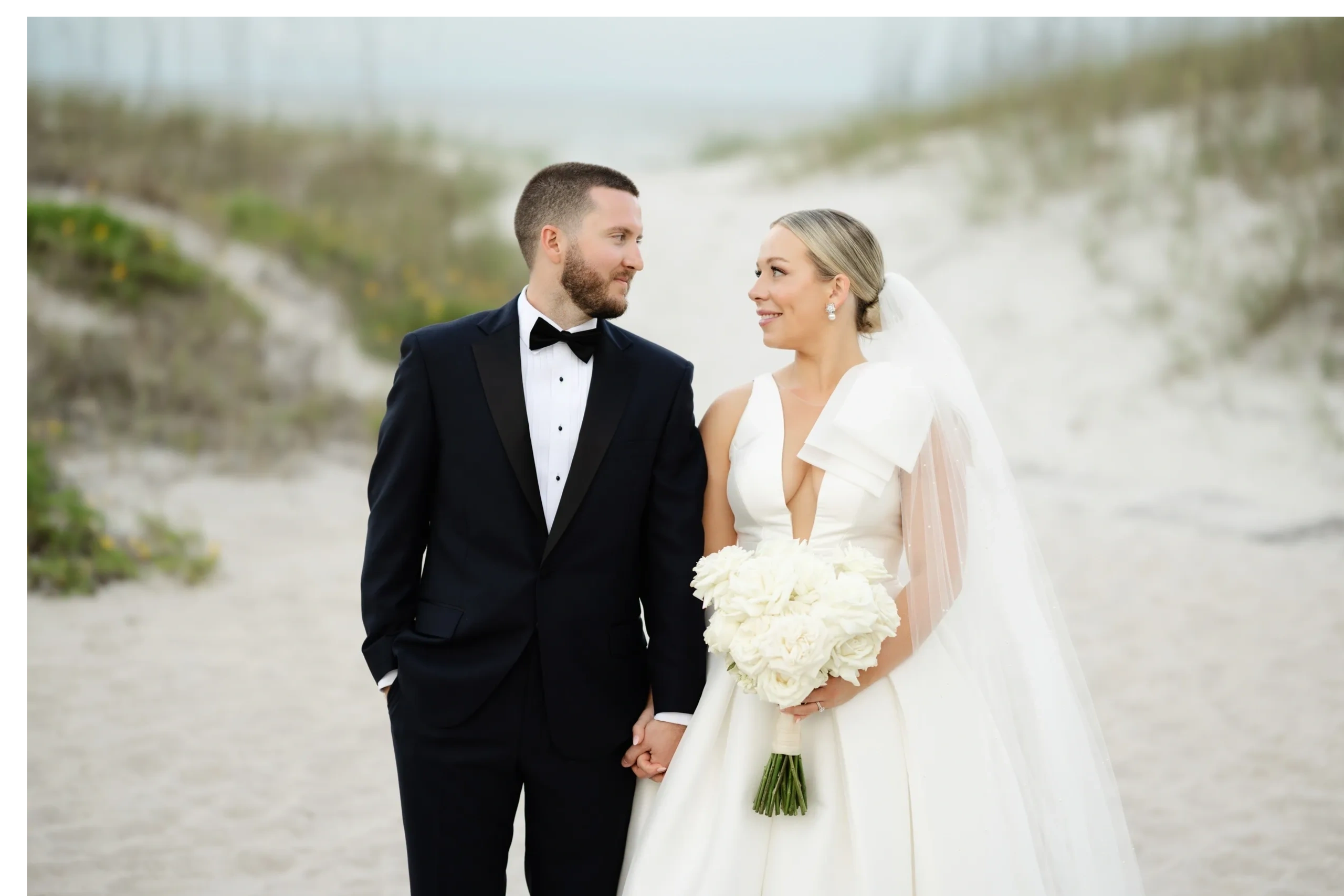 Bride and groom holding hands on sandy beach, destination wedding portrait