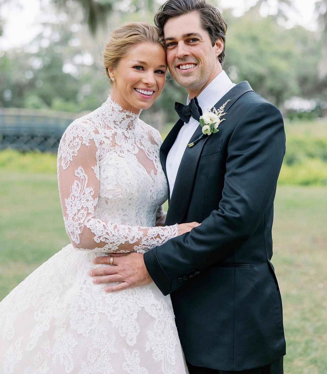 Bride in white lace long-sleeve gown with groom in navy tuxedo, garden portrait