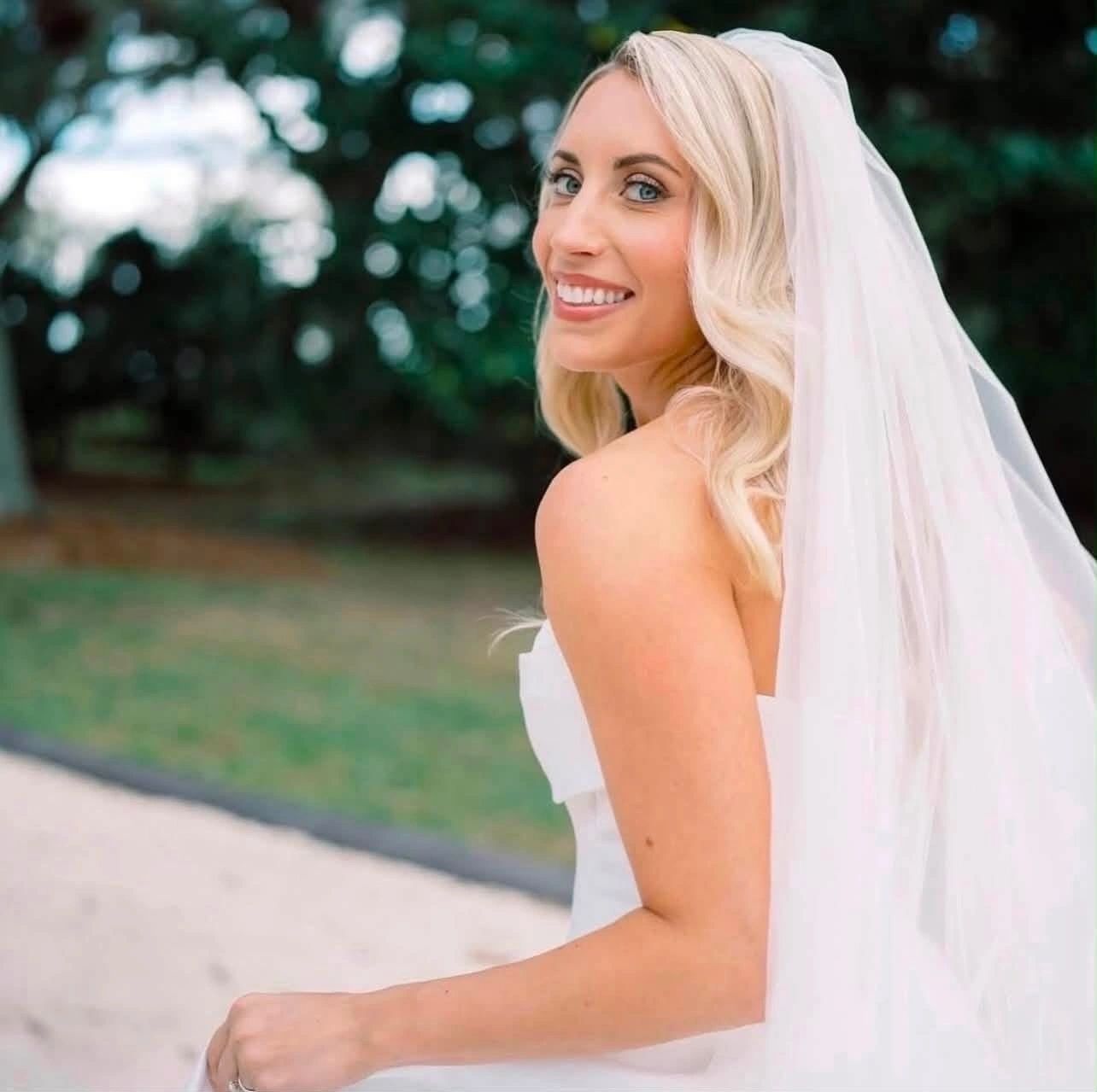 Bride in white gown and veil looking over shoulder in garden setting